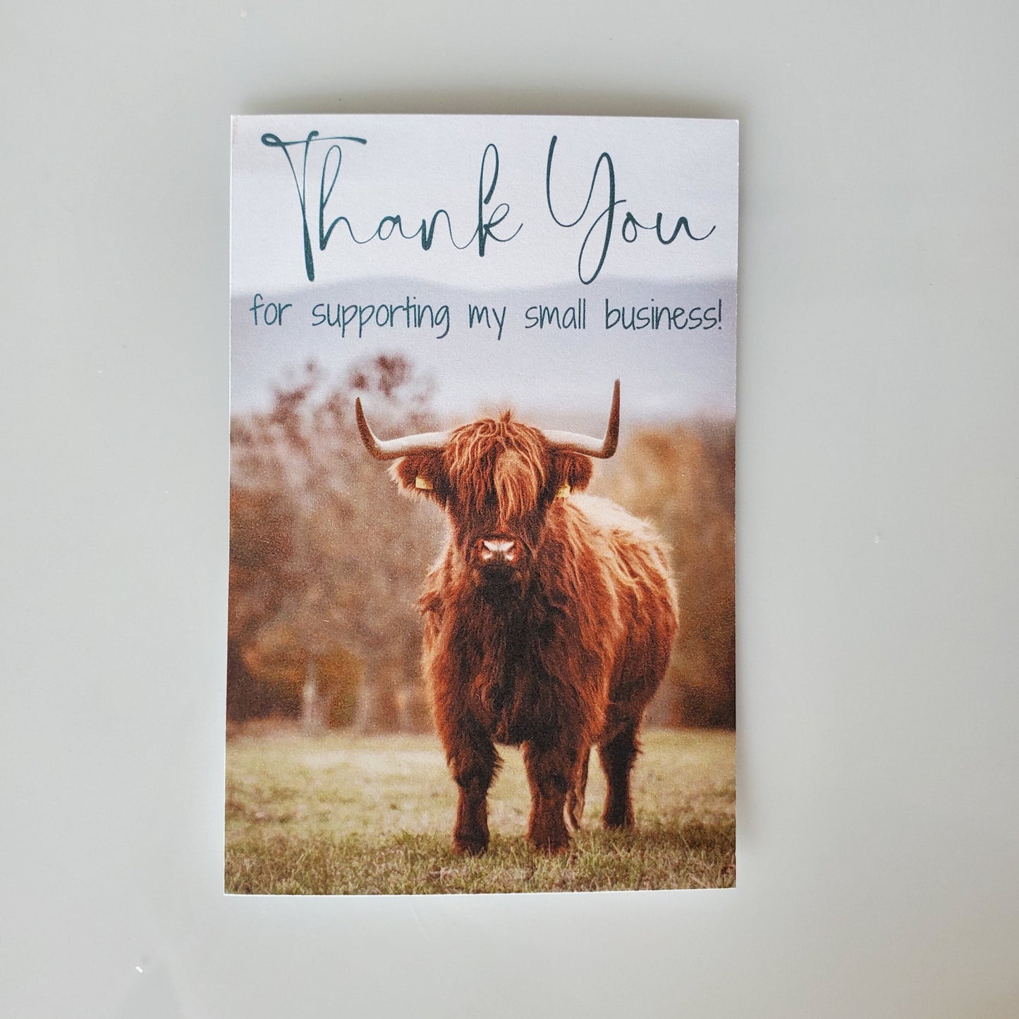card on a table, cow with horns standing in a field with trees in the background. Thank you for supporting my small business words on the top- confetti drop shop