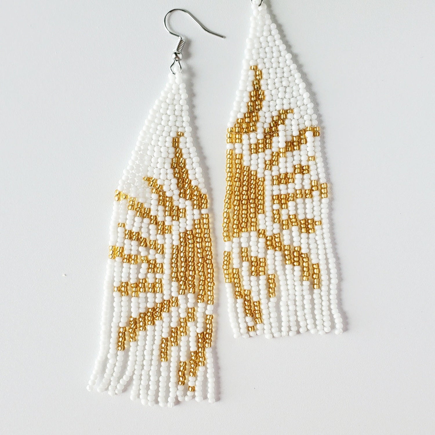 4.75" white seed beaded earrings with half a gold sun woven into each earring with a silver hook, laying on a white background