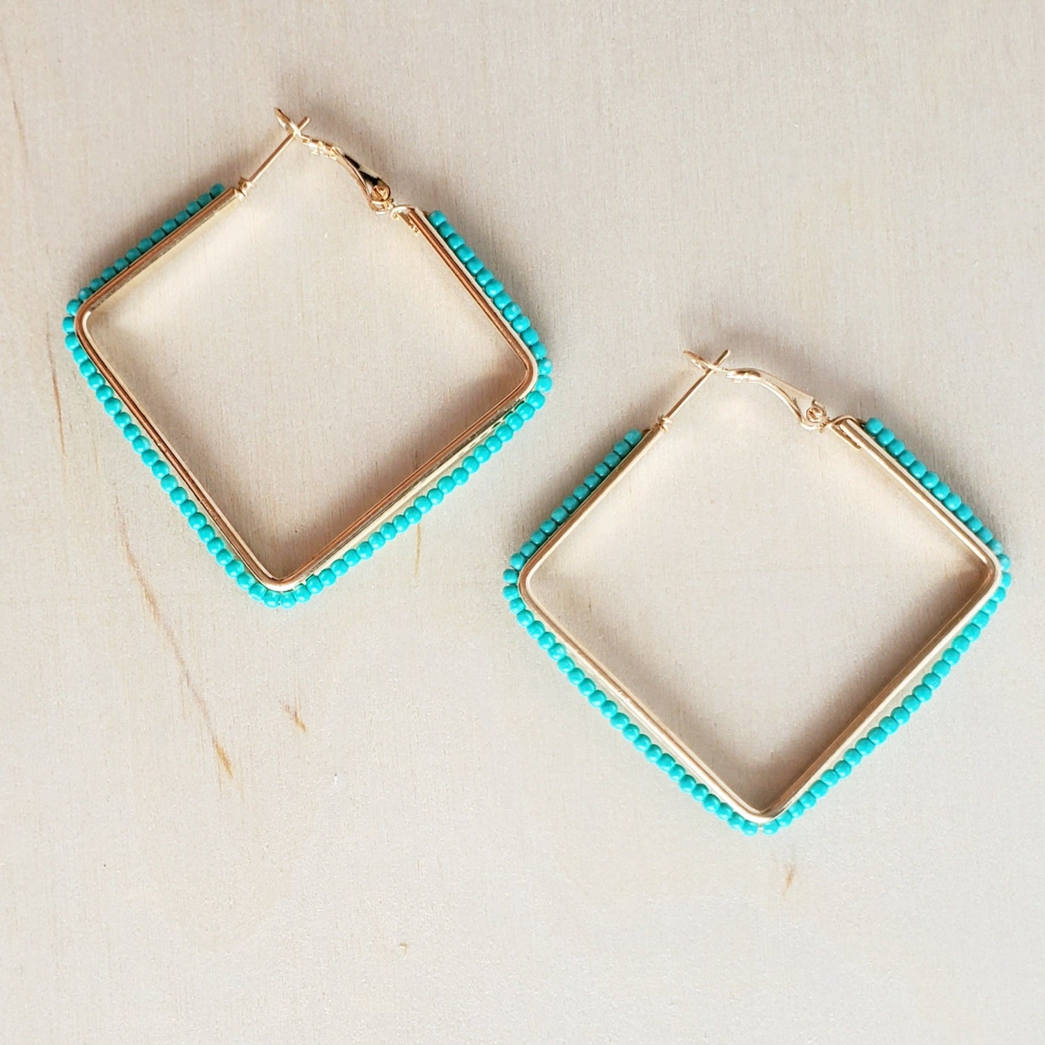 light wood background with square metal hinge back earrings lined with small turquoise beads