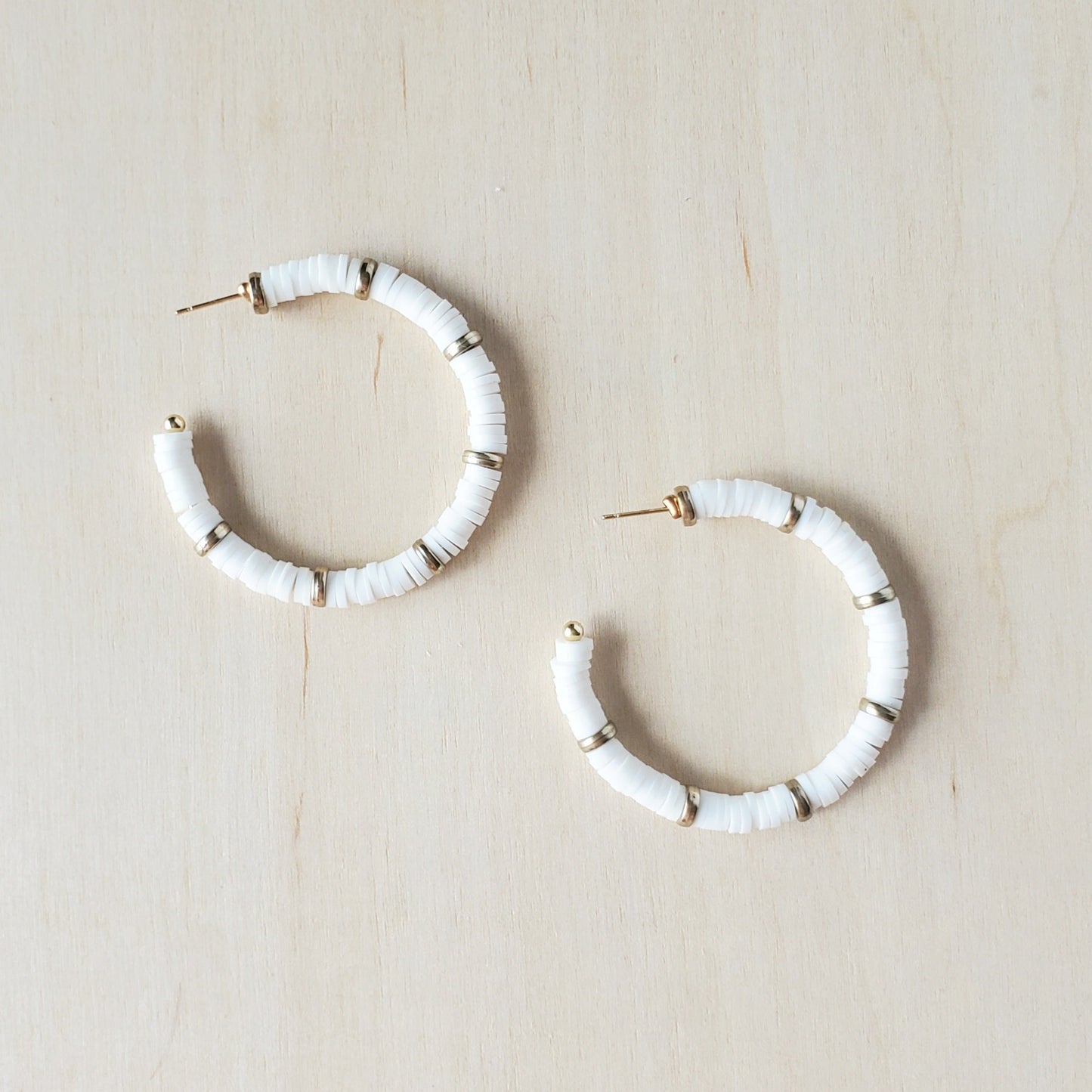A pair of white and gold polymer clay hoop earrings rest on a wooden background