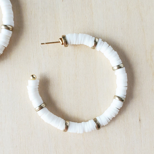 white polymer clay discs and flat gold beads make up  a medium hoop earring, resting on a wood background