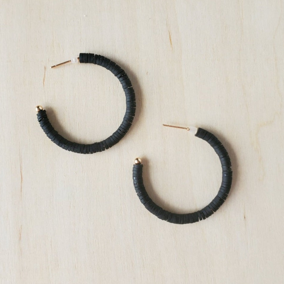 a pair of black polymer clay disk hoop earrings on a wooden table