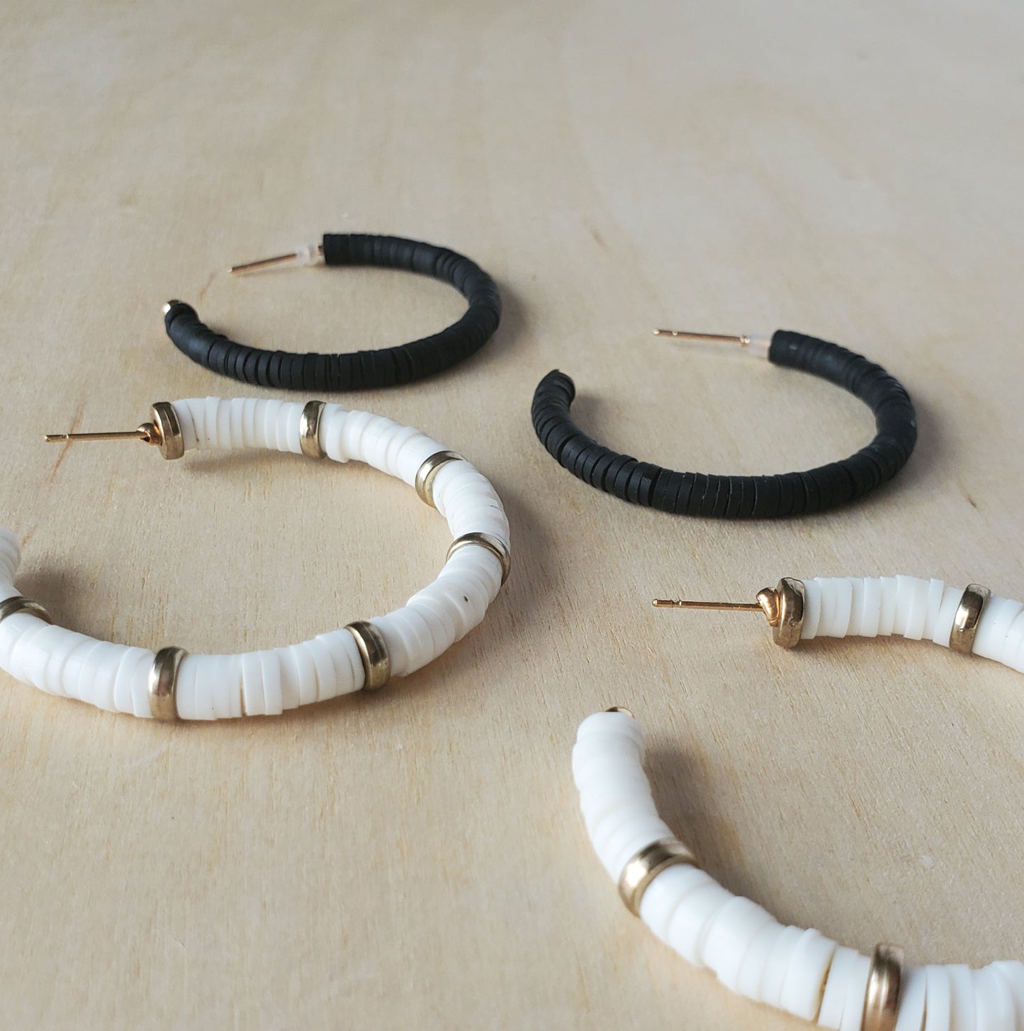 a pair of black and a pair of white and gold polymer clay disc hoop earrings resting on a natural wood table